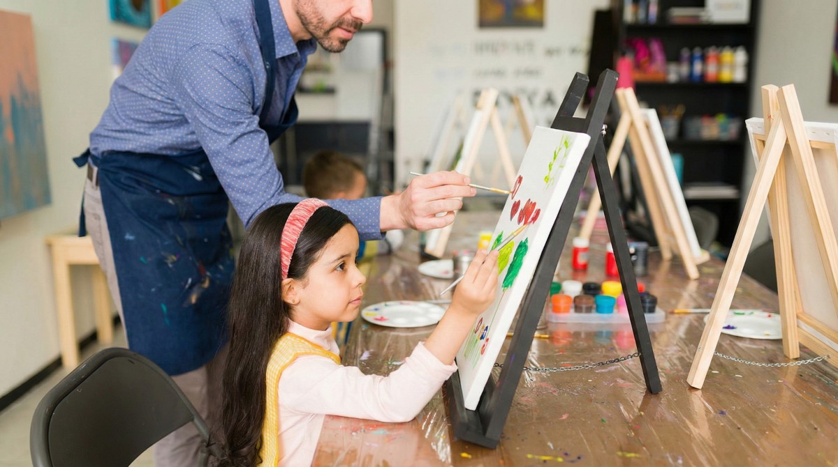 Art teacher guiding a young child during a creative painting class to improve focus and self-discipline